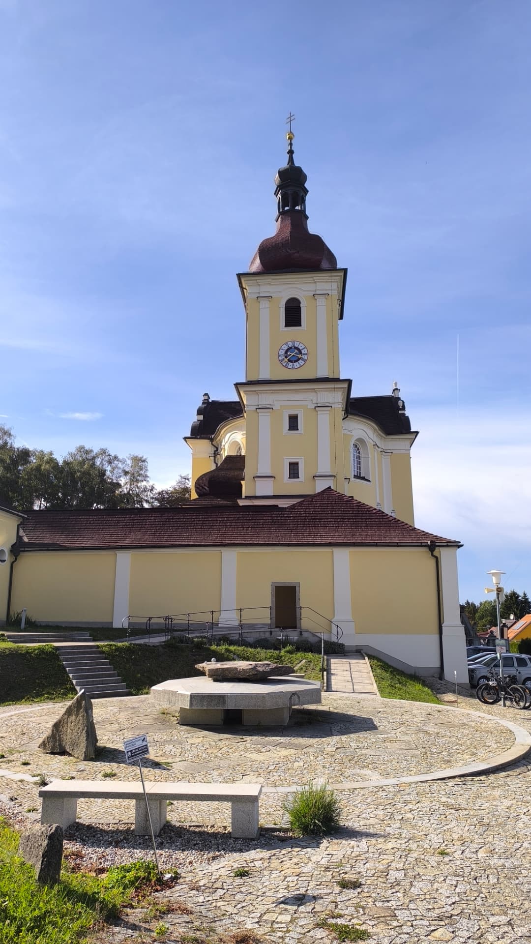 Pohled na kostel na Dobré Vodě od východu s místem k posezení a kamenným stolem