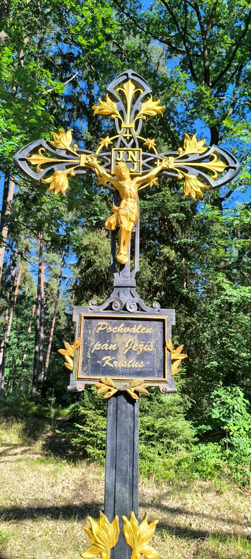 Detail bohatě zdobeného kříže s nápisem Pochválen pán Ježíš Kristus