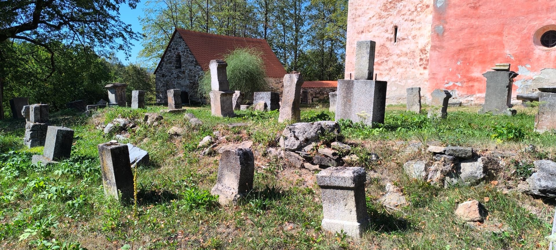 Zbytky starého hřbitova s kamennými patkami náhrobků a márnicí u kostela