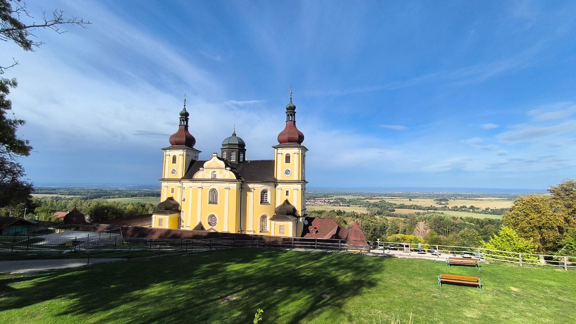 Poutní kostel na Dobré Vodě z teras nad ním s lavičkami a dalekým výhledem do krajiny