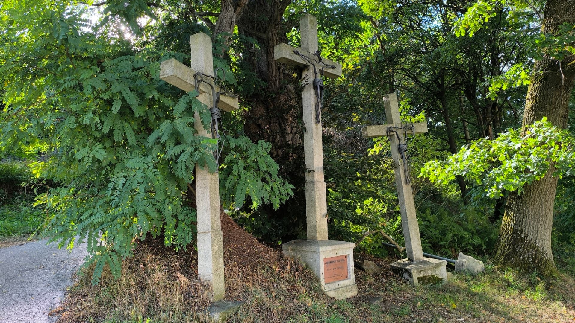 Tři kamenné kříže vedle sebe u cesty — památník obětem teroristických útoků z 11. září 2001 na Dobré Vodě